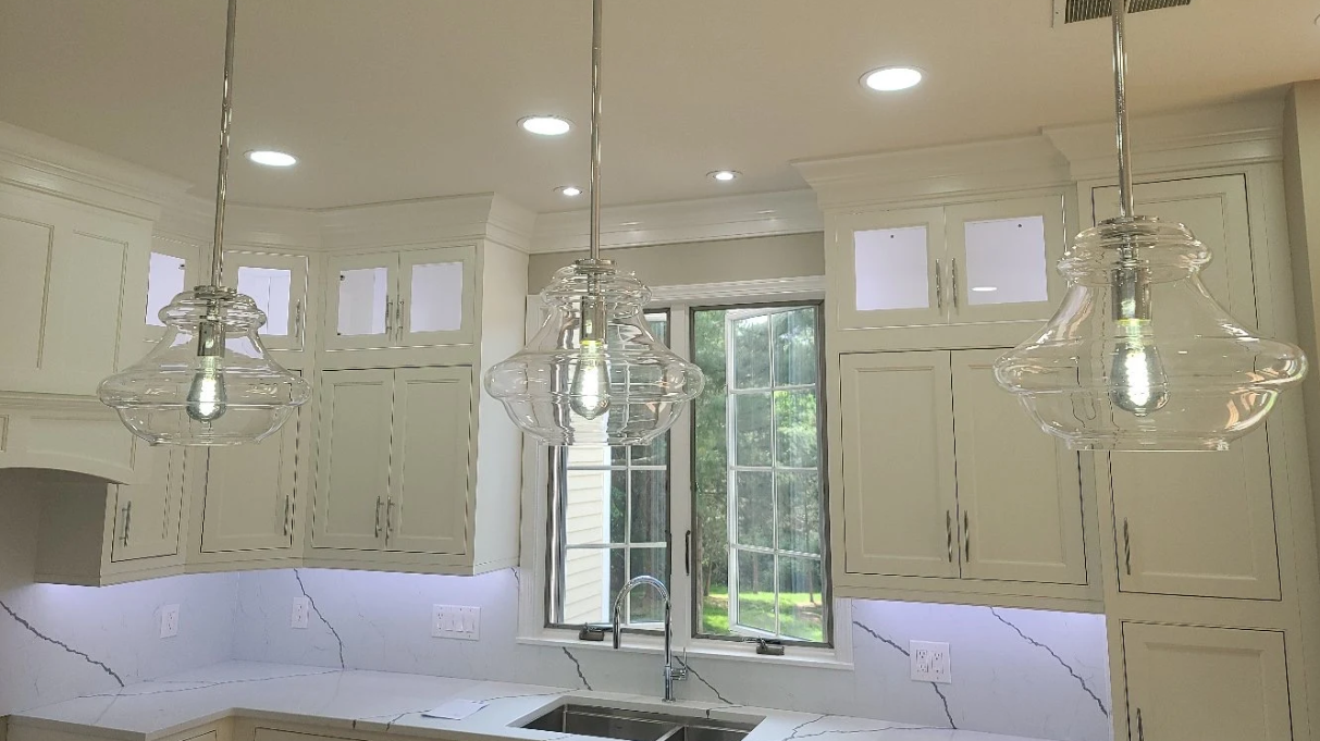 White kitchen with three glass pendant lights above a countertop, with a window in the center.