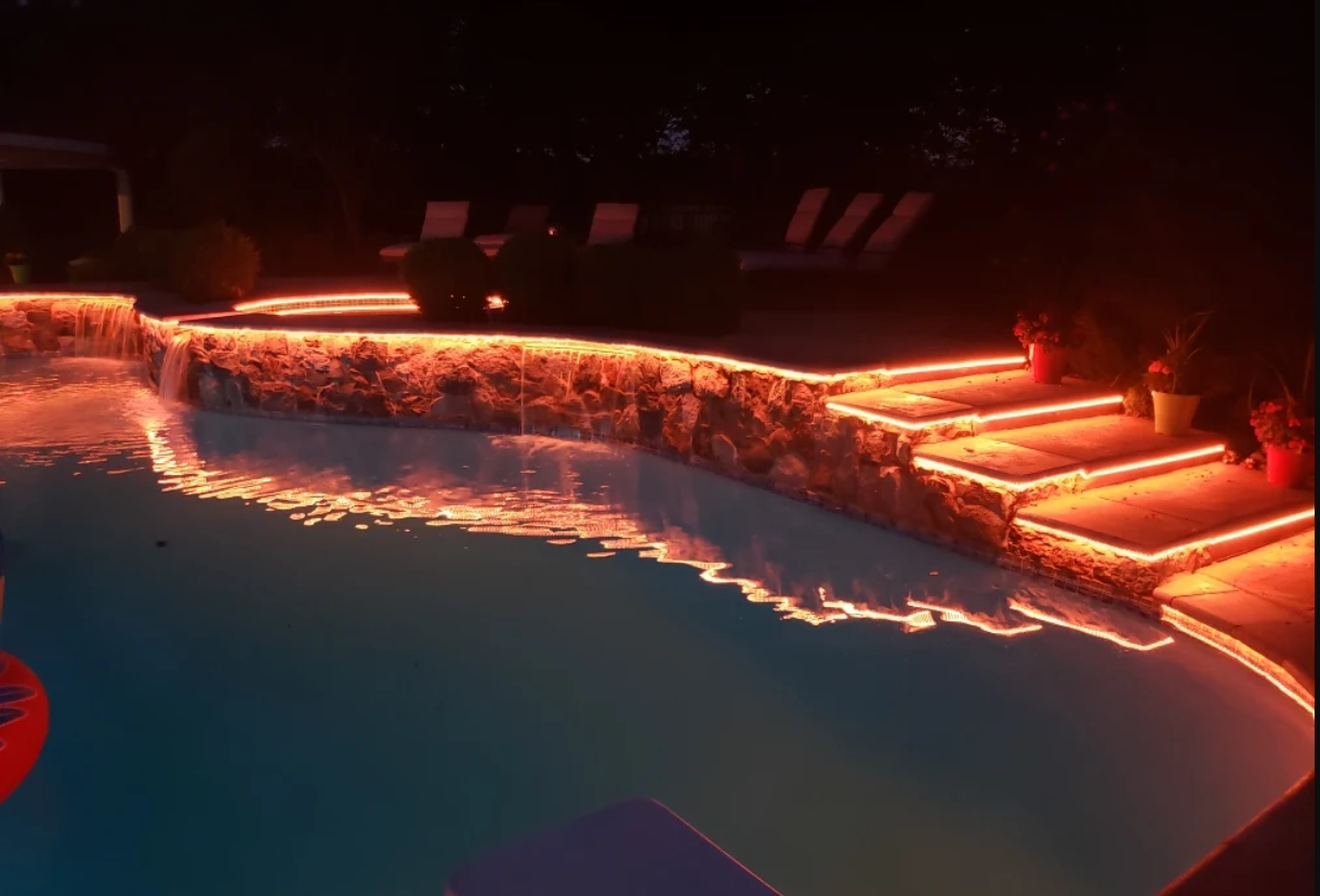 Pool with orange lights outlining the edges and steps, reflecting on the water at night.