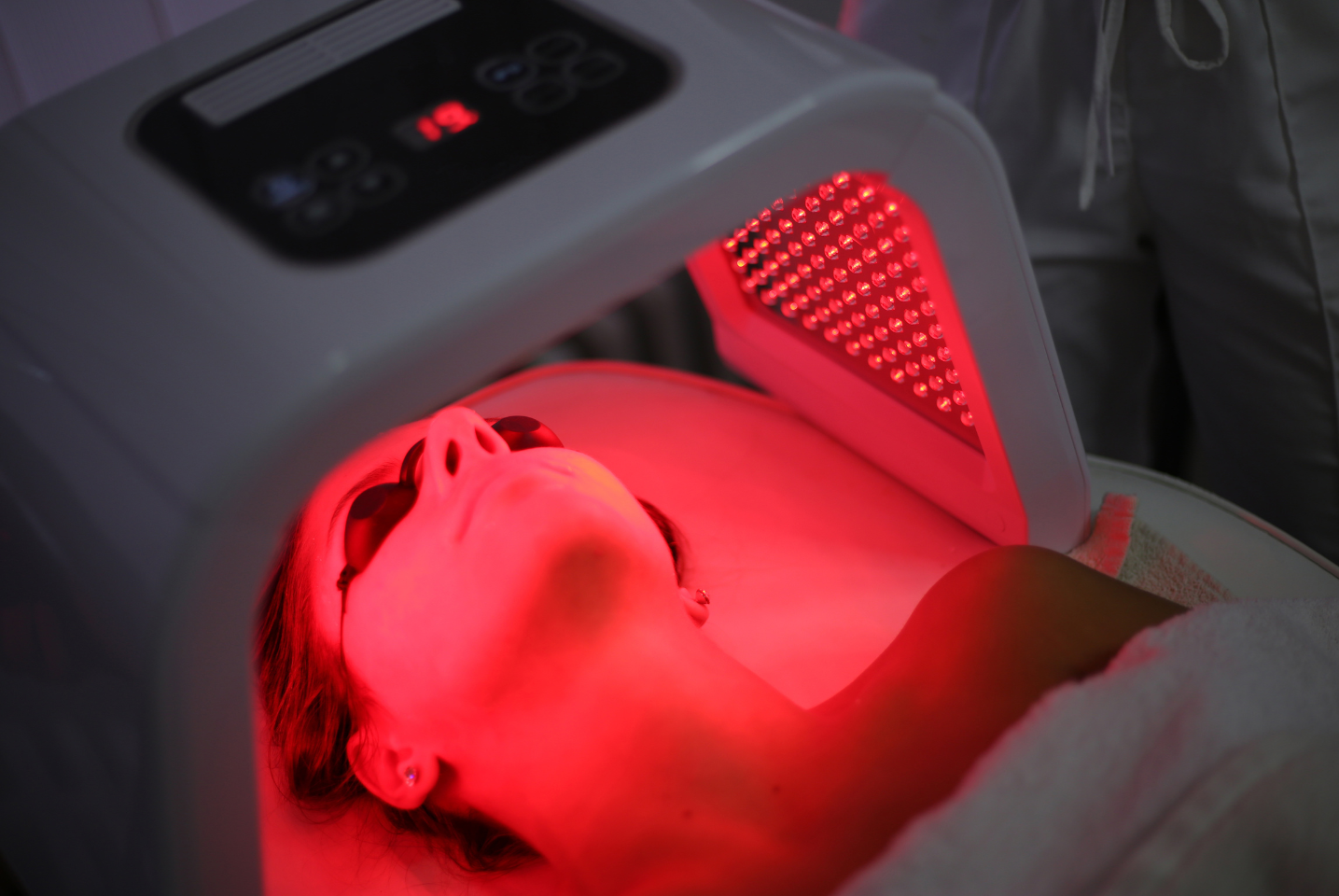 A person is laying on a bed with a led mask on their face.