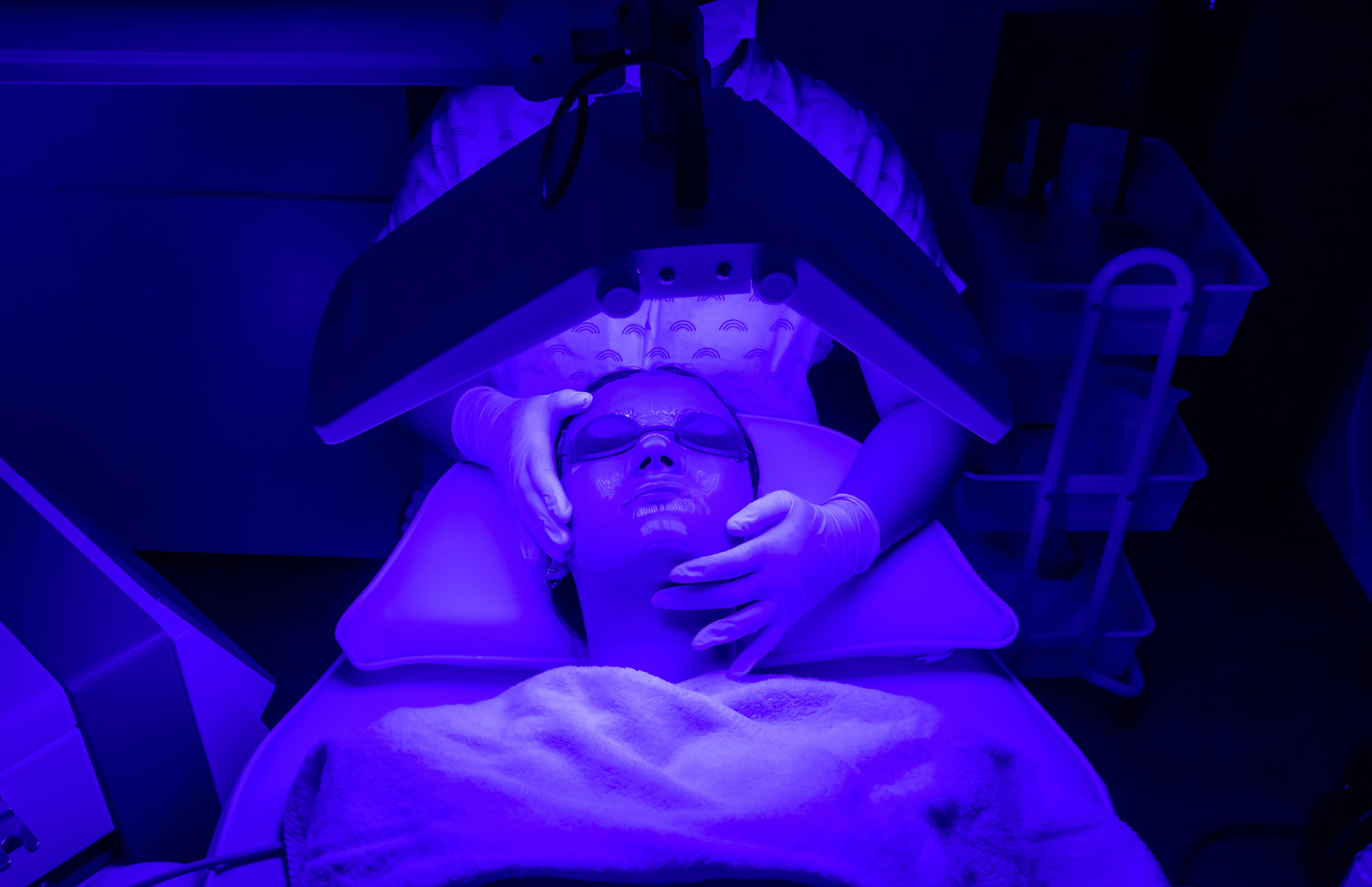 A woman wearing a mask is getting a blue light treatment on her face