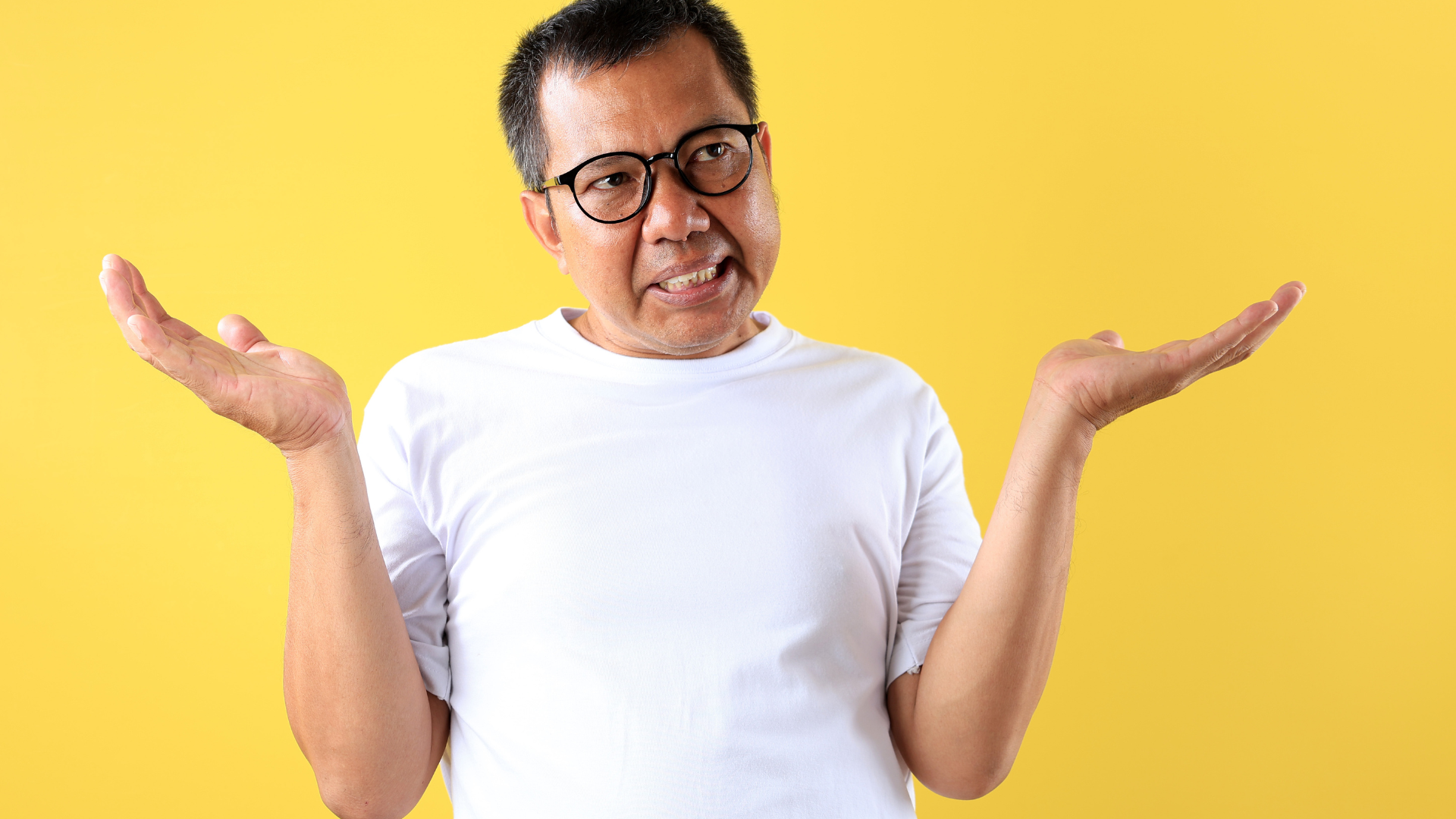 A man wearing glasses and a white shirt is shrugging his shoulders.