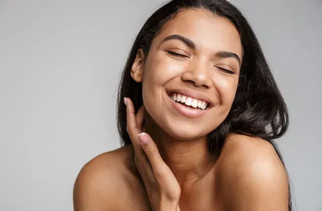 A woman is smiling and touching her face with her hand.