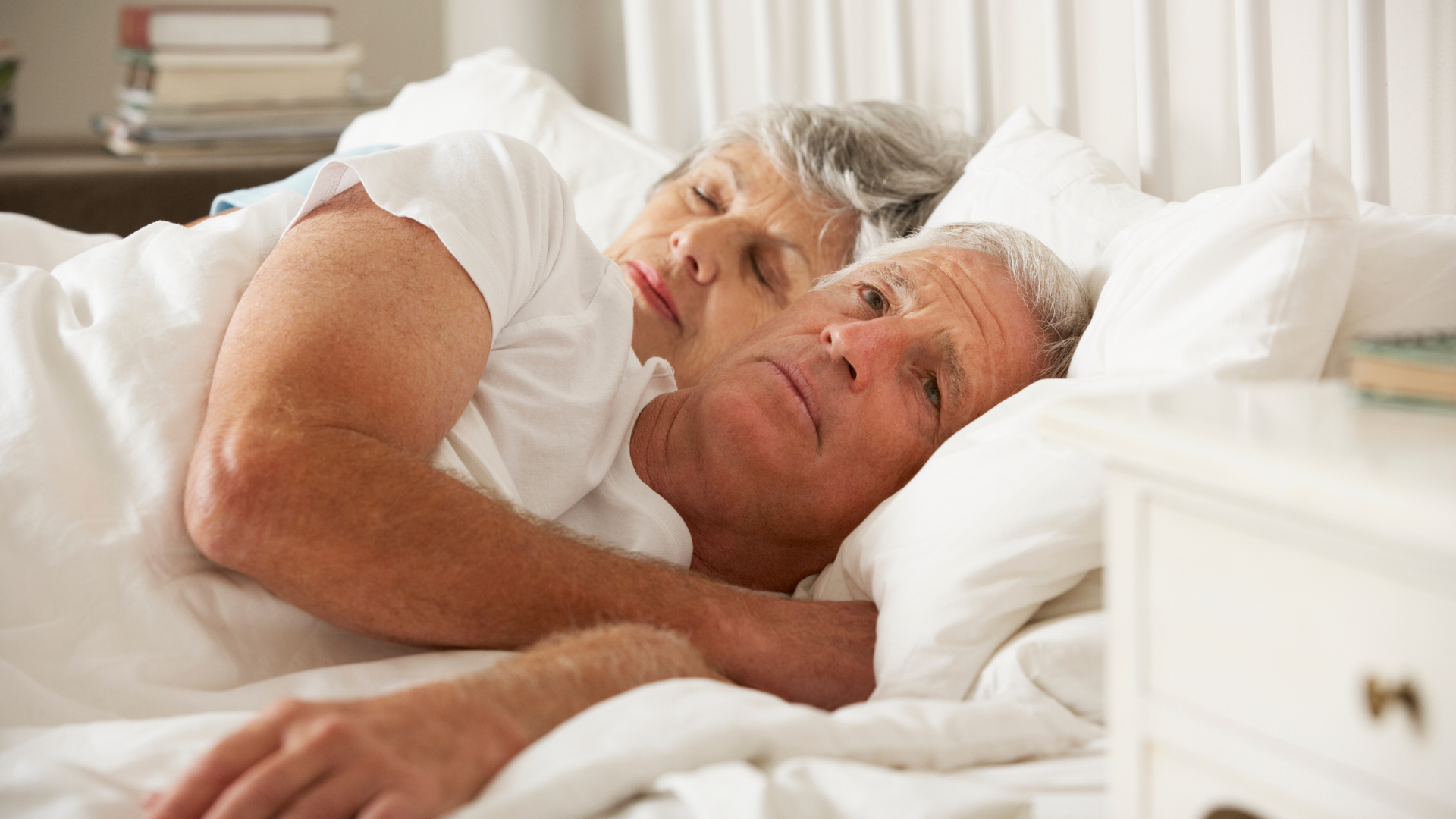 An elderly couple is sleeping in a bed together.