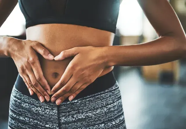 A woman is making a heart shape with her hands on her stomach.
