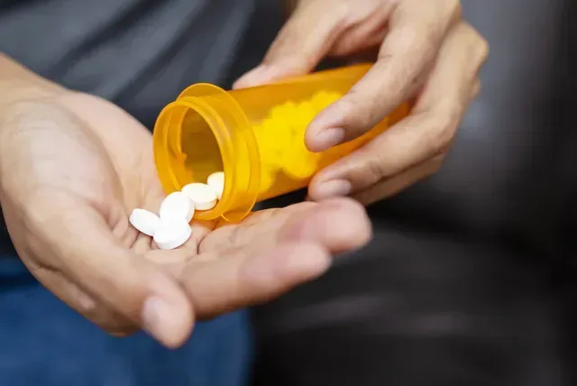 A person is pouring pills from a bottle into their hand.