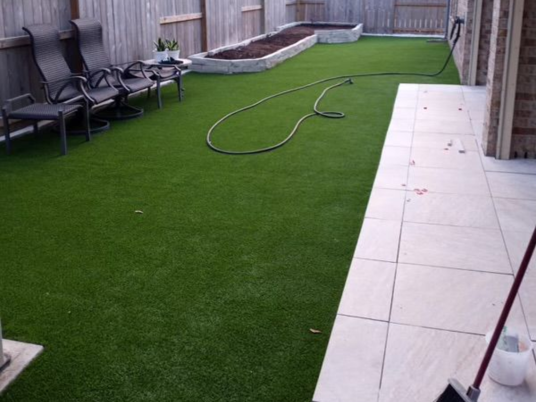 Backyard with artificial green turf, patio, black chairs, and a raised garden bed.