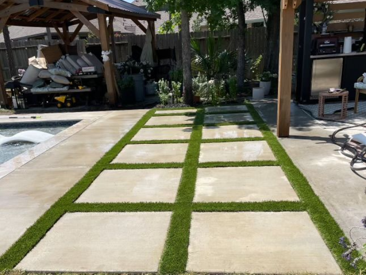 Concrete pavers with green grass in a backyard by a pool.
