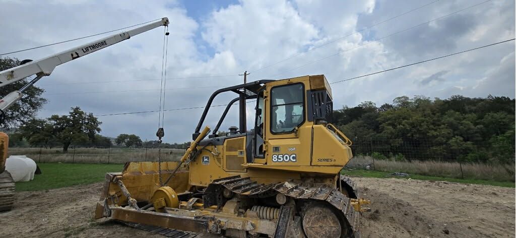 A yellow bulldozer is parked in a dirt field next to a crane.
