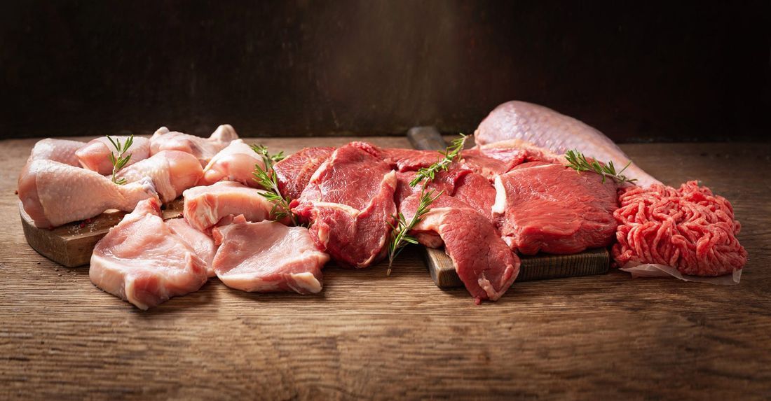 Assortimento di tagli di manzo crudo su un tagliere di legno con guarnizione di erbe aromatiche e cipolla.
