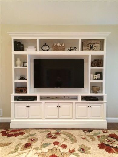 White built-in entertainment center with open shelving, cabinets, and a mounted TV. A floral rug is in front.