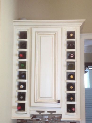 White cabinet with wine racks on either side of a central door; holding multiple wine bottles.