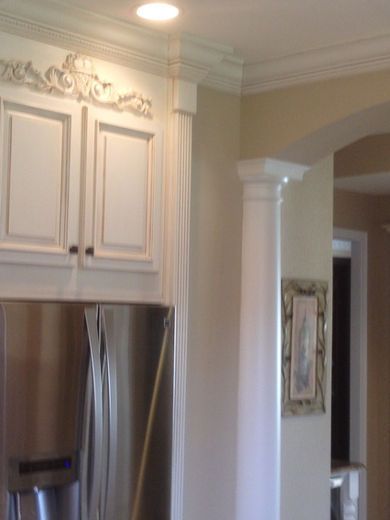 White kitchen cabinets with stainless steel refrigerator and decorative molding.