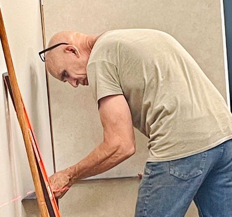 Bald man in glasses installing a wood plank with a laser level, indoors.
