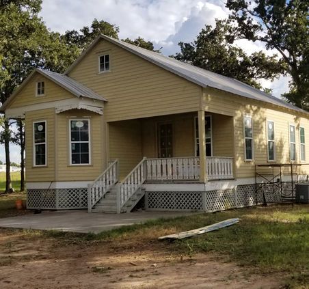 Yellow house with porch, white trim, metal roof, under construction.