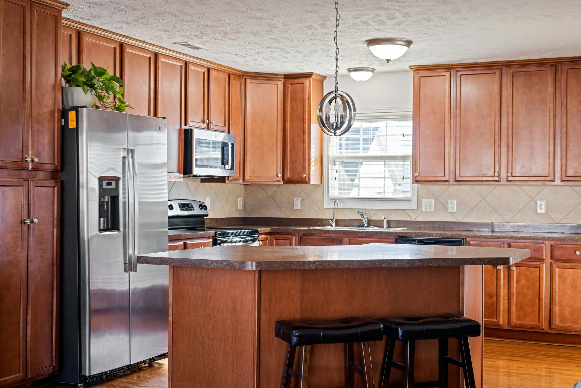 Kitchen with brown cabinets, stainless steel refrigerator, island with seating, and a window.