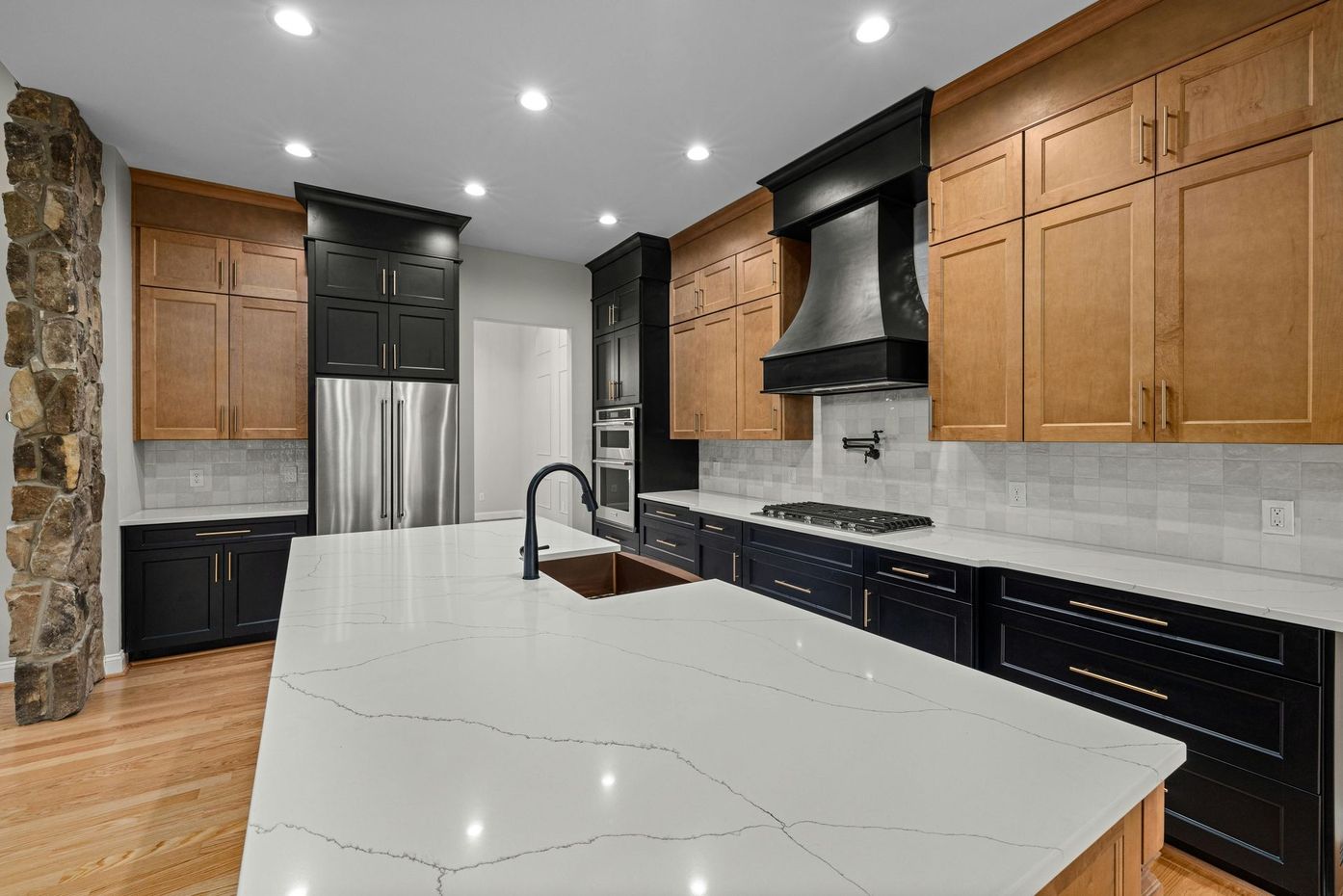 Modern kitchen with black and wood cabinets, large island with white countertop, and stainless steel appliances.