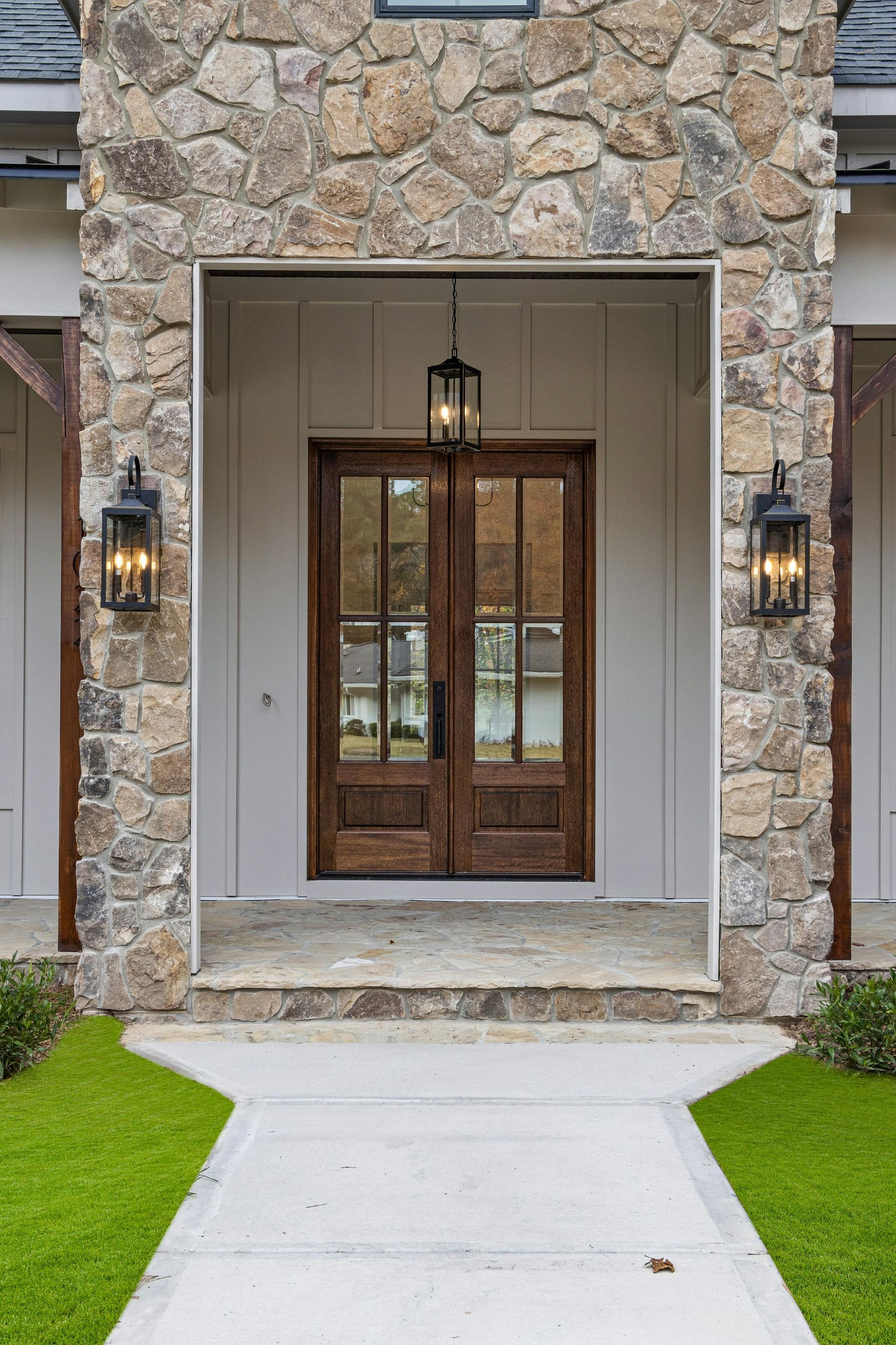 Stone entryway with double brown doors, flanked by black lanterns. A walkway leads to the entrance.