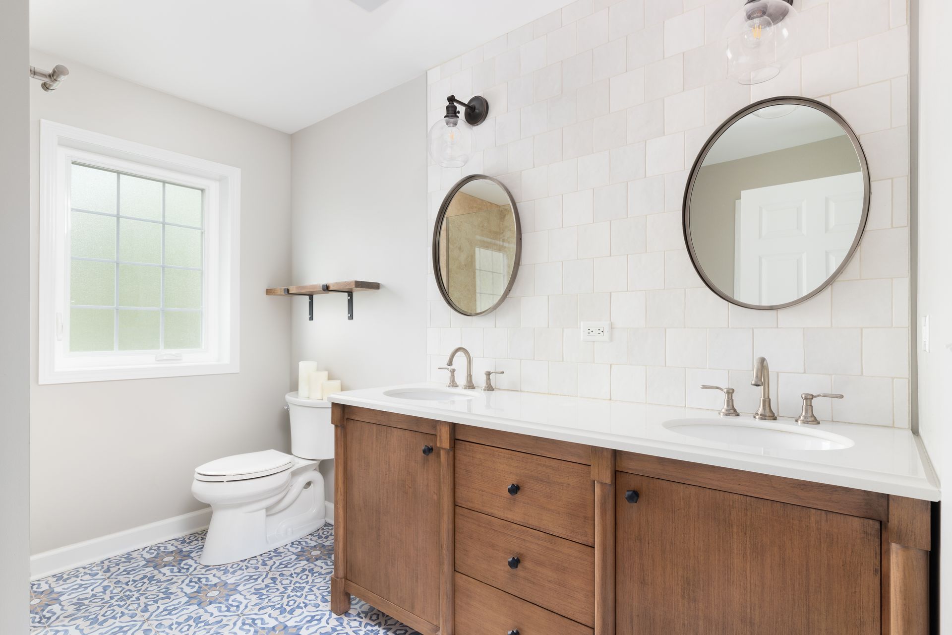Bathroom with double vanity, oval mirrors, white tile wall, and patterned blue floor.