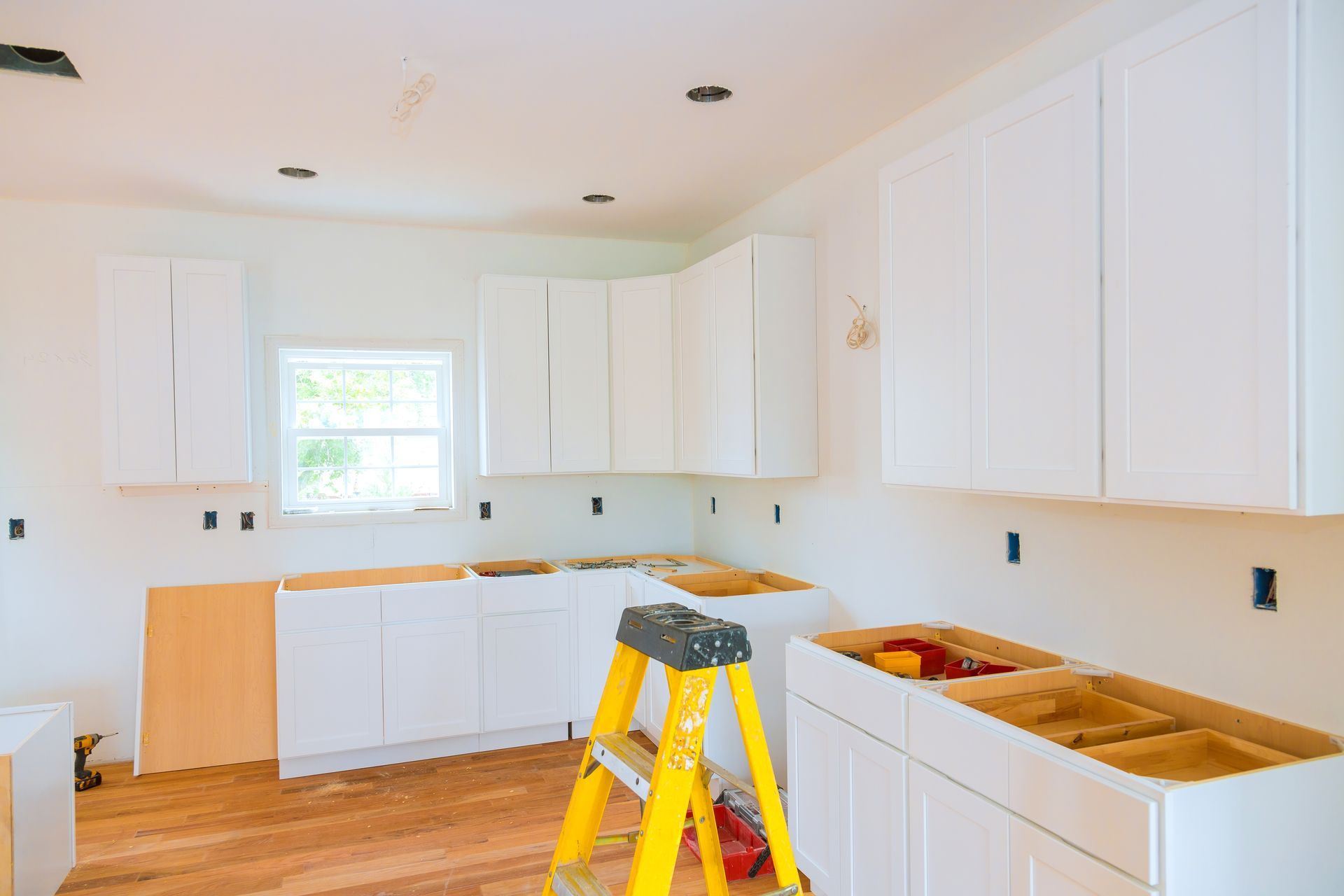 Kitchen under renovation, white cabinets, wooden countertops, and a yellow ladder.