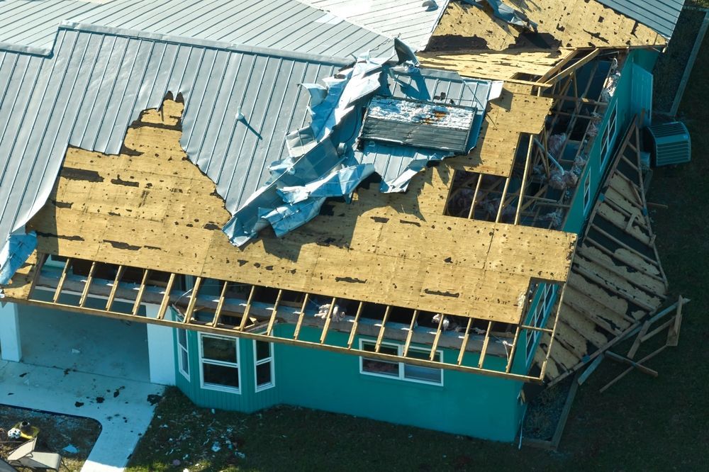 House with significant roof damage, turquoise siding, and exposed wood framing.