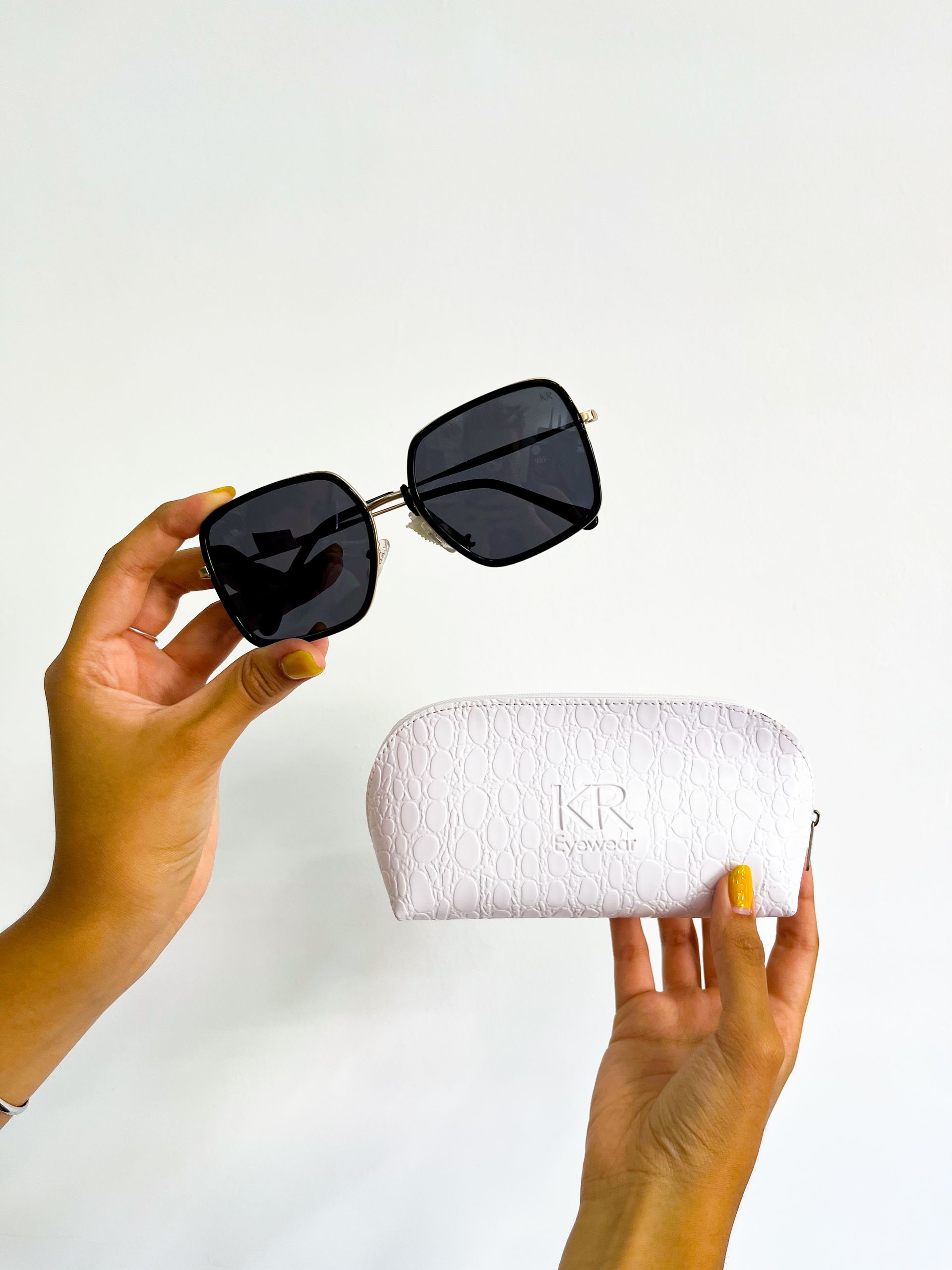 Manos sosteniendo gafas de sol sobre un estuche de gafas blanco, contra un fondo blanco.