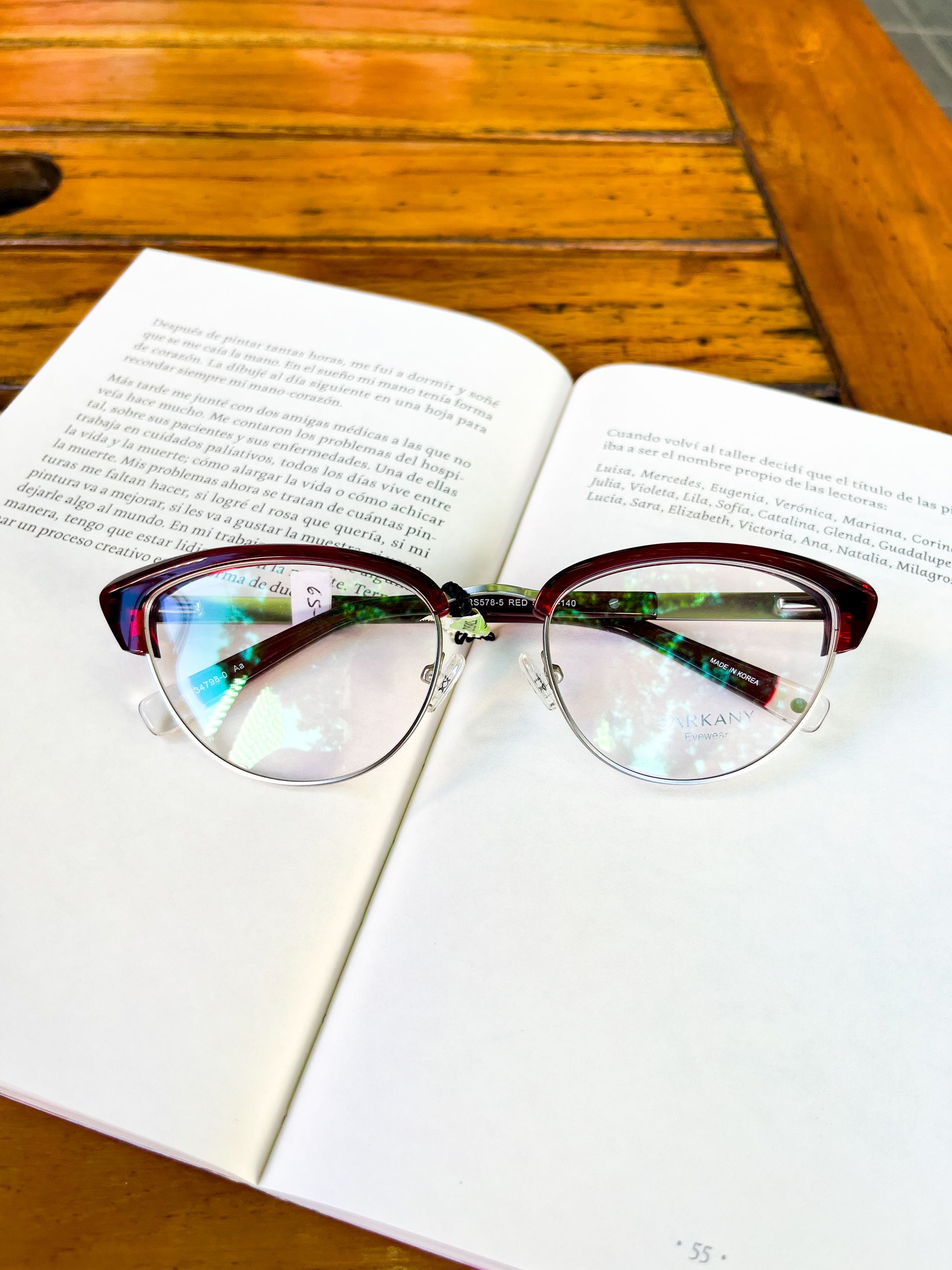 Unas gafas con borde superior de color rojo oscuro y marco plateado descansan sobre un libro abierto