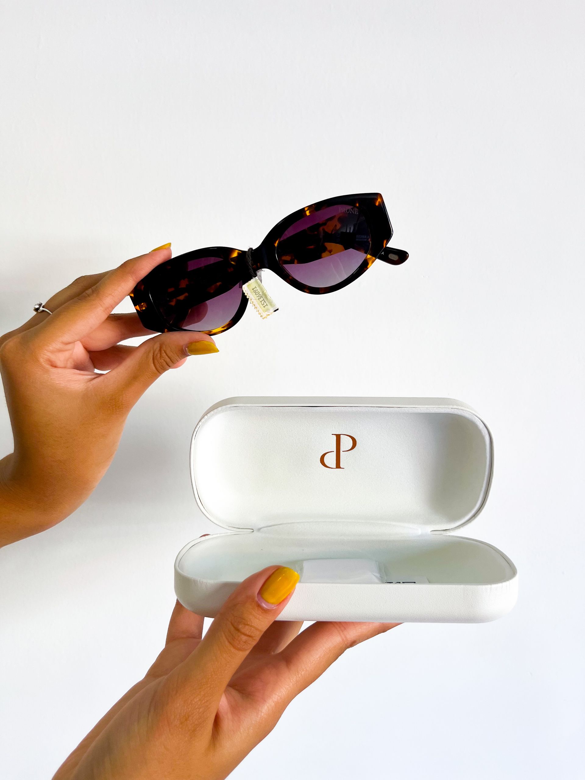 Persona sosteniendo unas gafas de sol de color carey sobre un estuche de gafas blanco abierto.