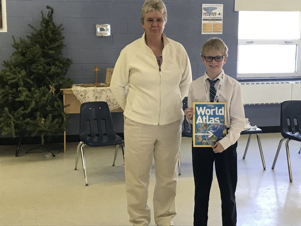A woman stands next to a boy holding a world atlas