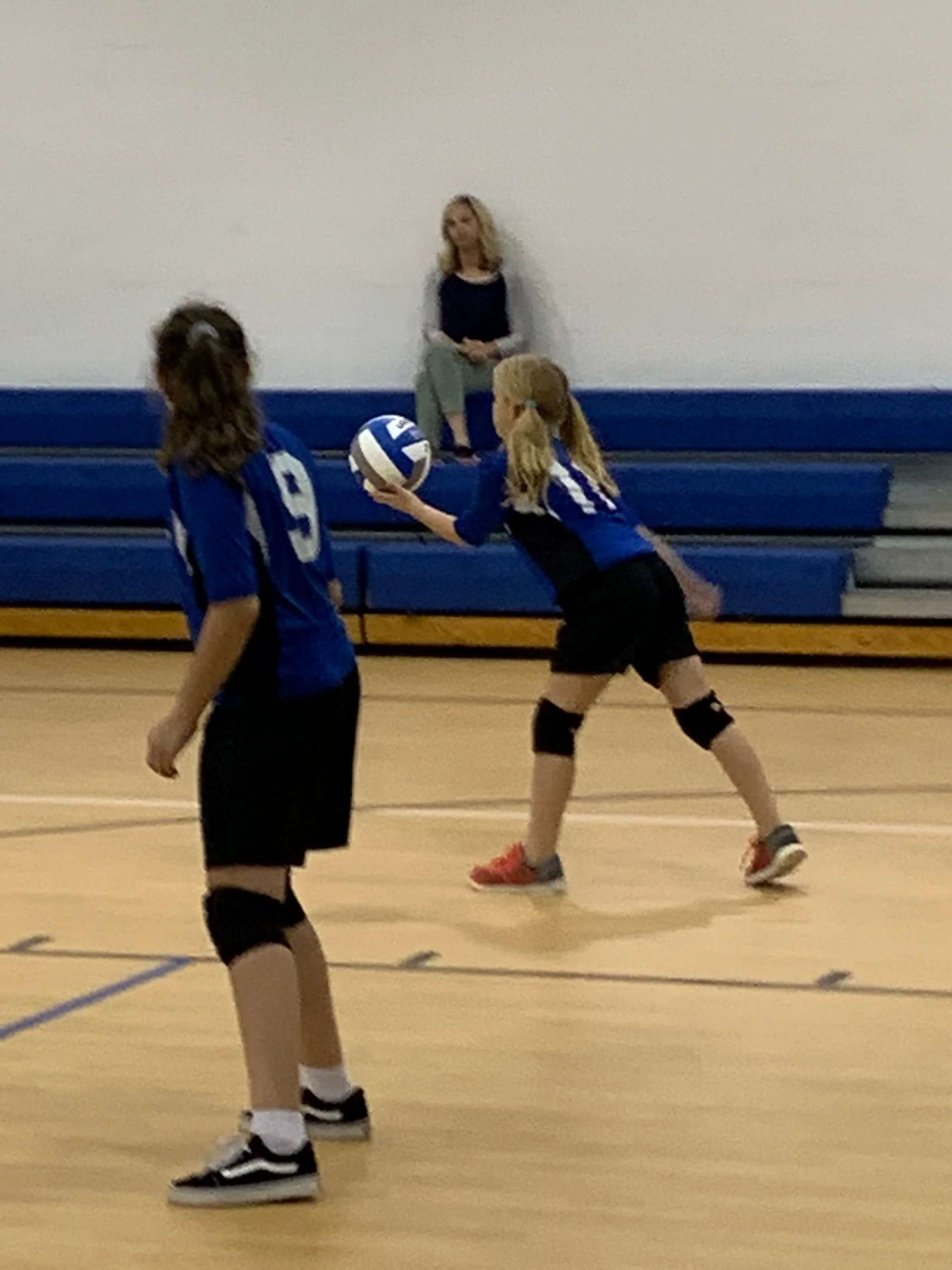 Two girls are playing volleyball while a mom watches them.