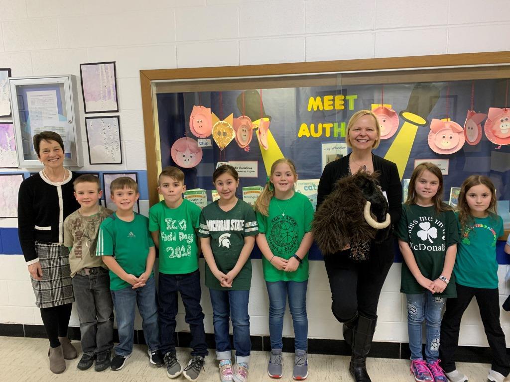 A group of children standing in front of a bulletin board that says meet author