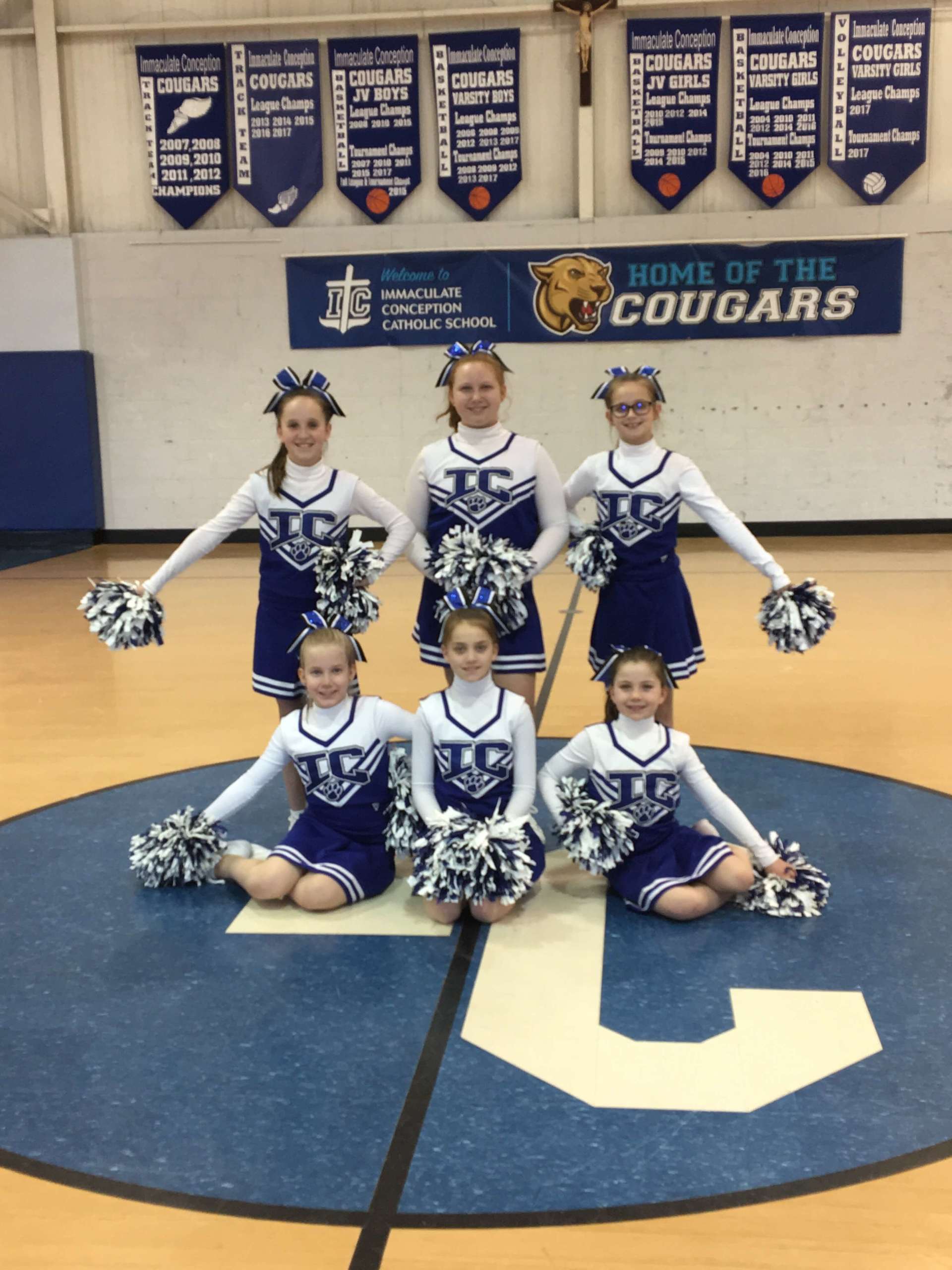Cheerleaders pose in front of a sign that says Home of the Cougars.