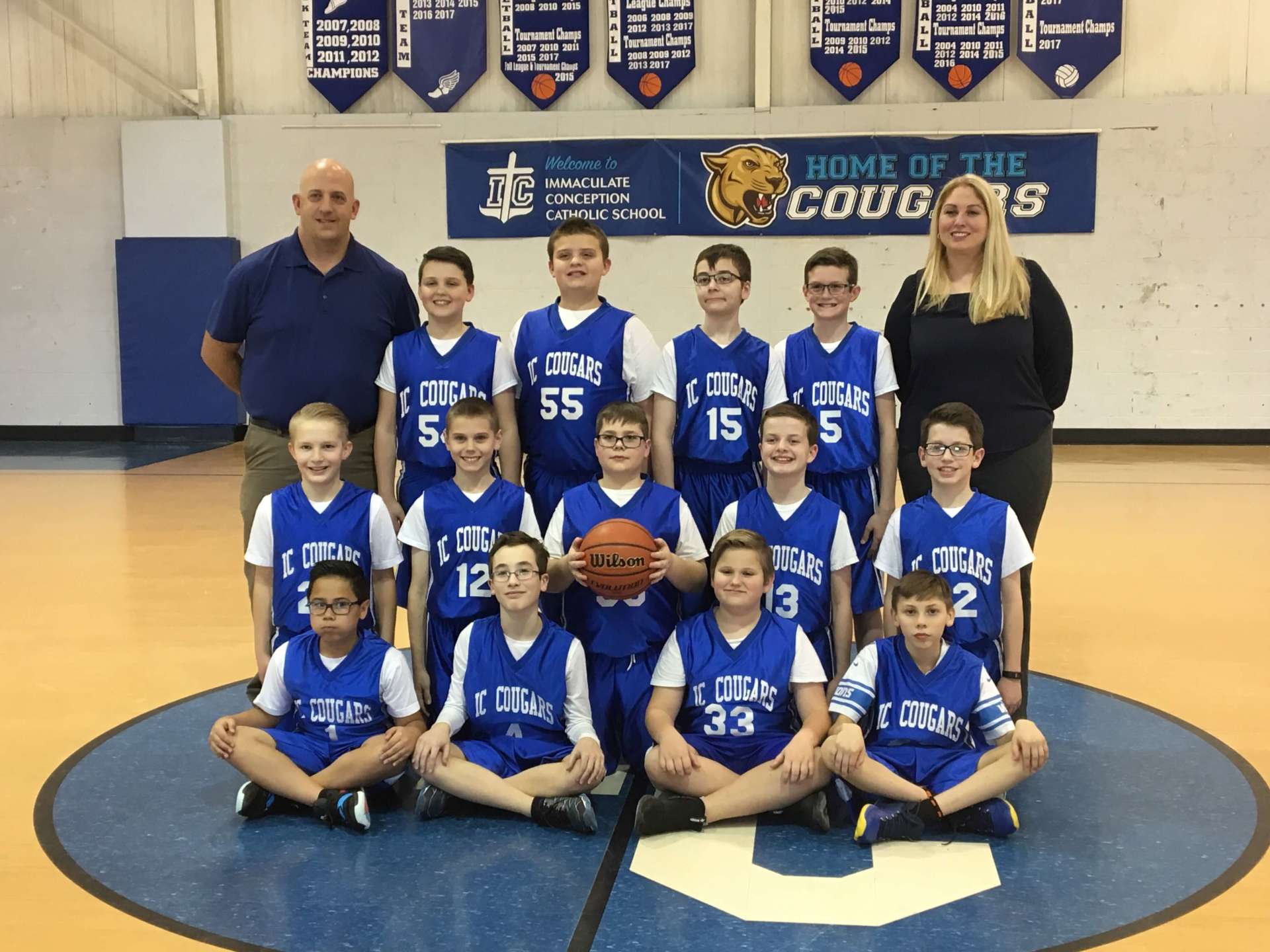 A basketball team poses in front of a banner that says Home of the Cougars.