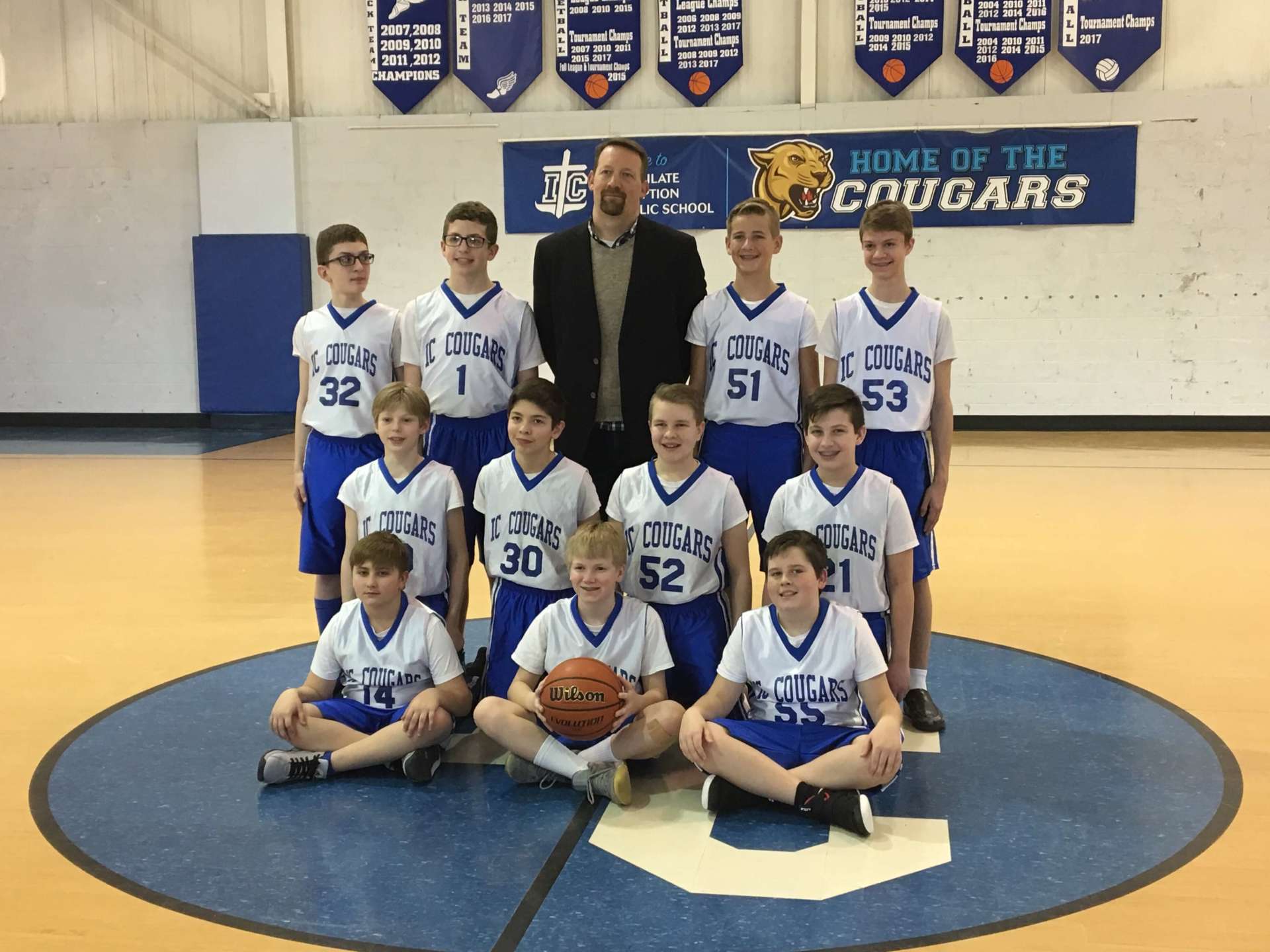 A basketball team poses for a photo in front of a sign that says Home of the Cougars.
