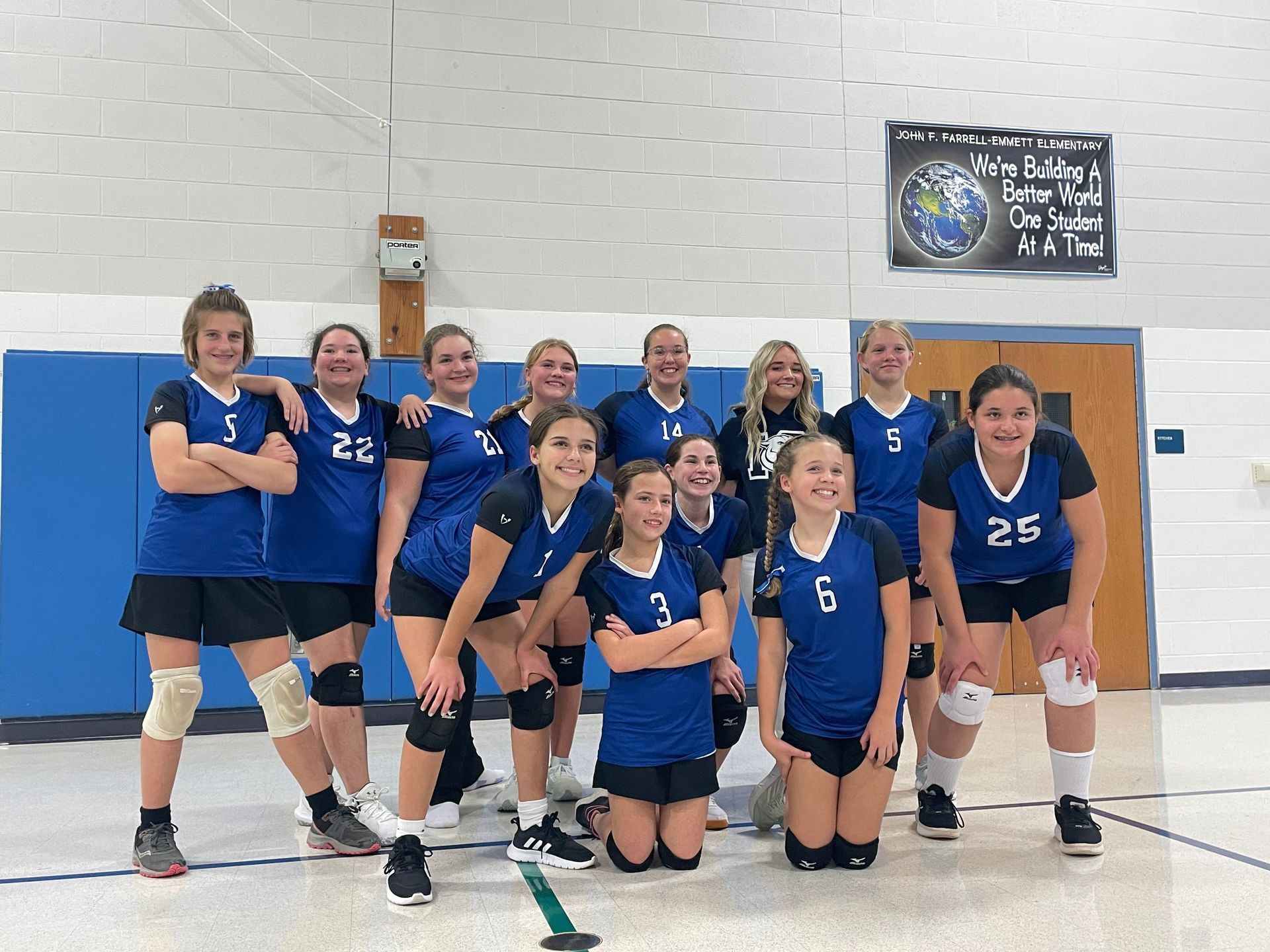 A volleyball team poses in front of a sign that says; 