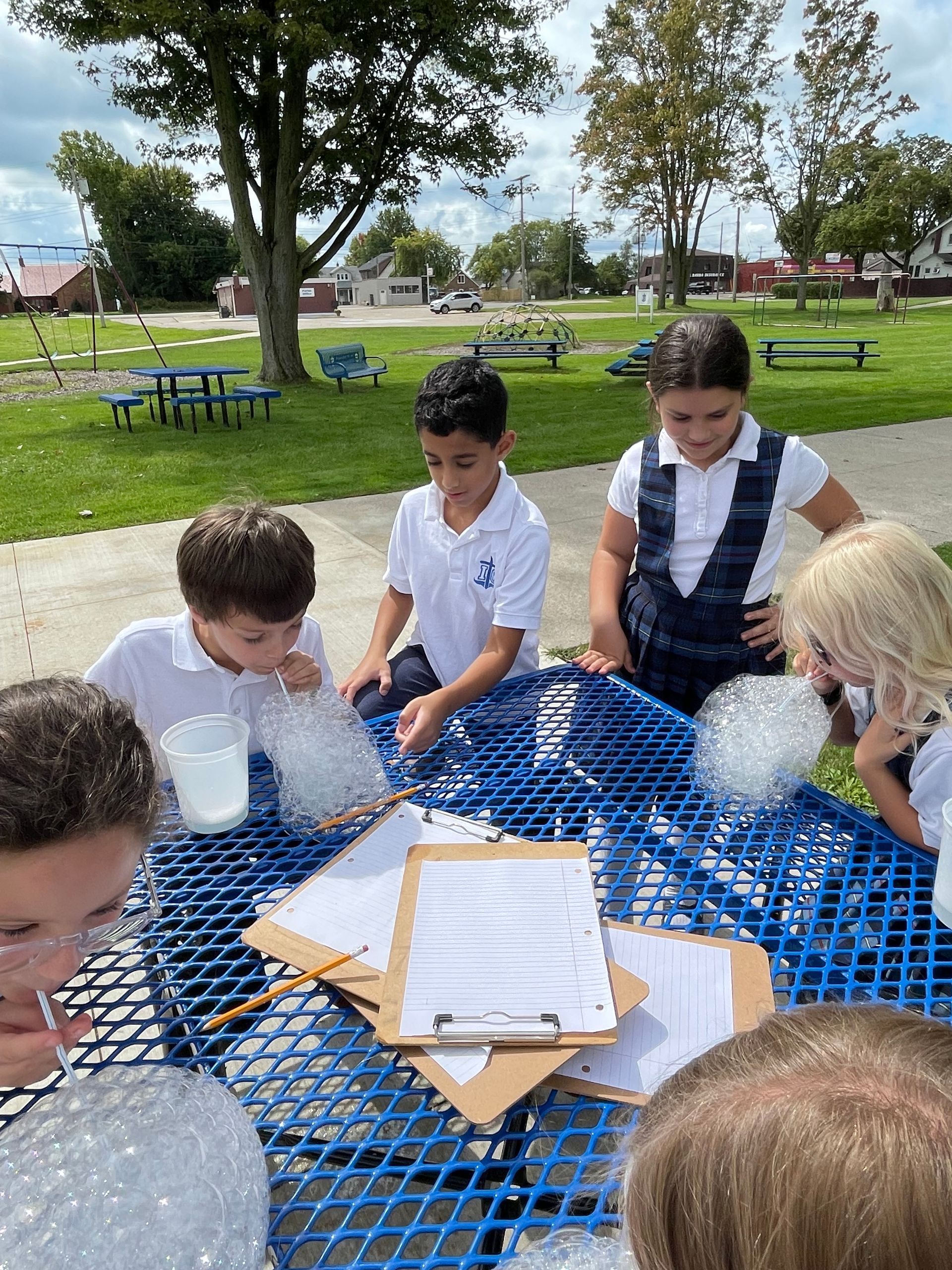 A group of children are sitting at a blue picnic table blowing bubbles.