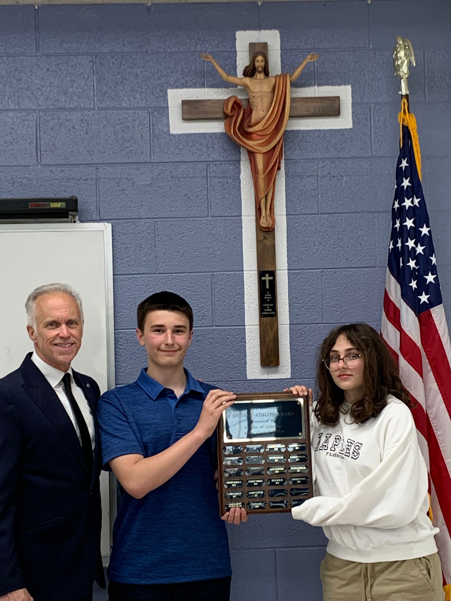 Students and staff hold a plaque in front of a crucifix.
