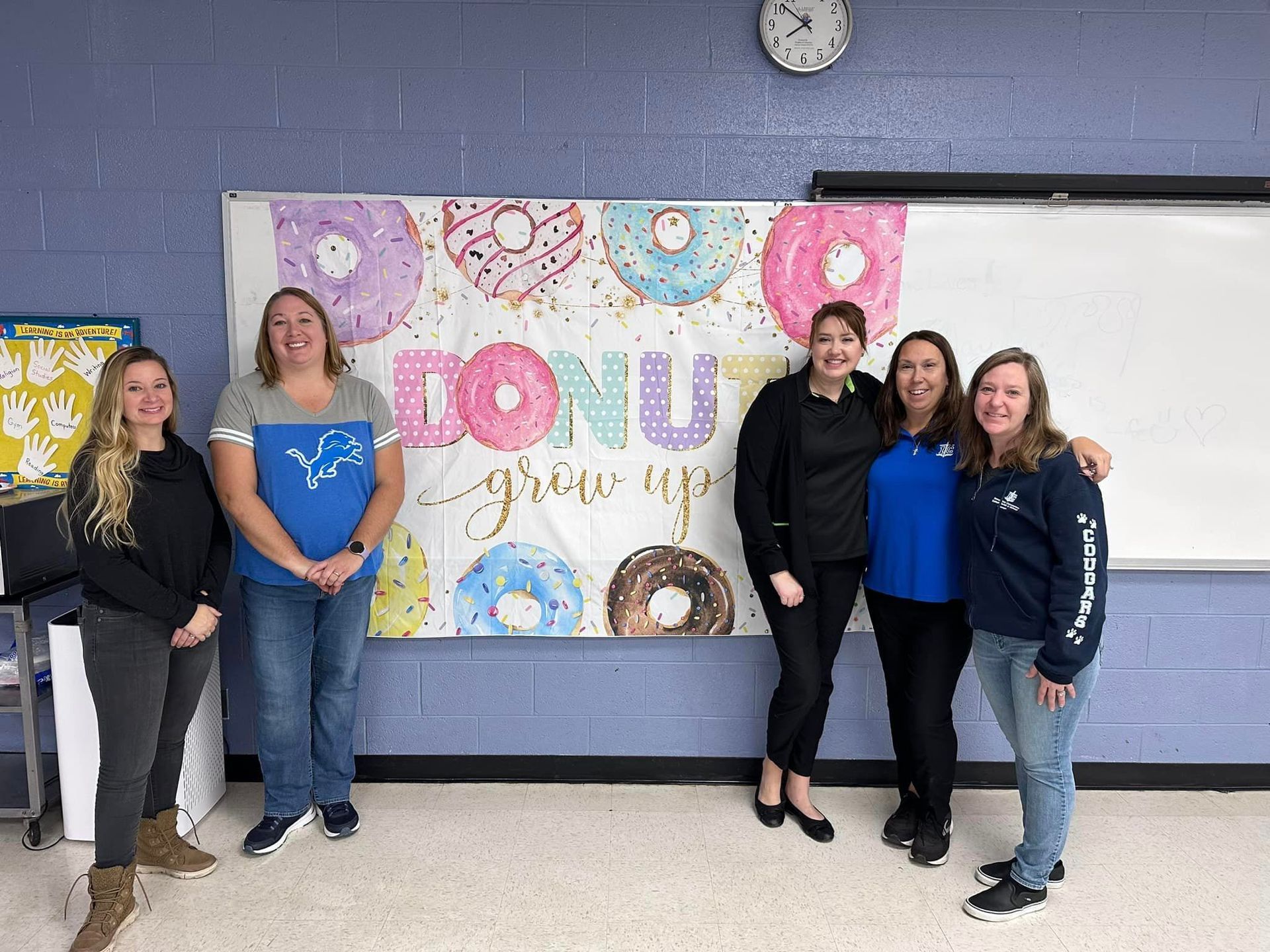 a group of women standing in front of a donut grow up sign.