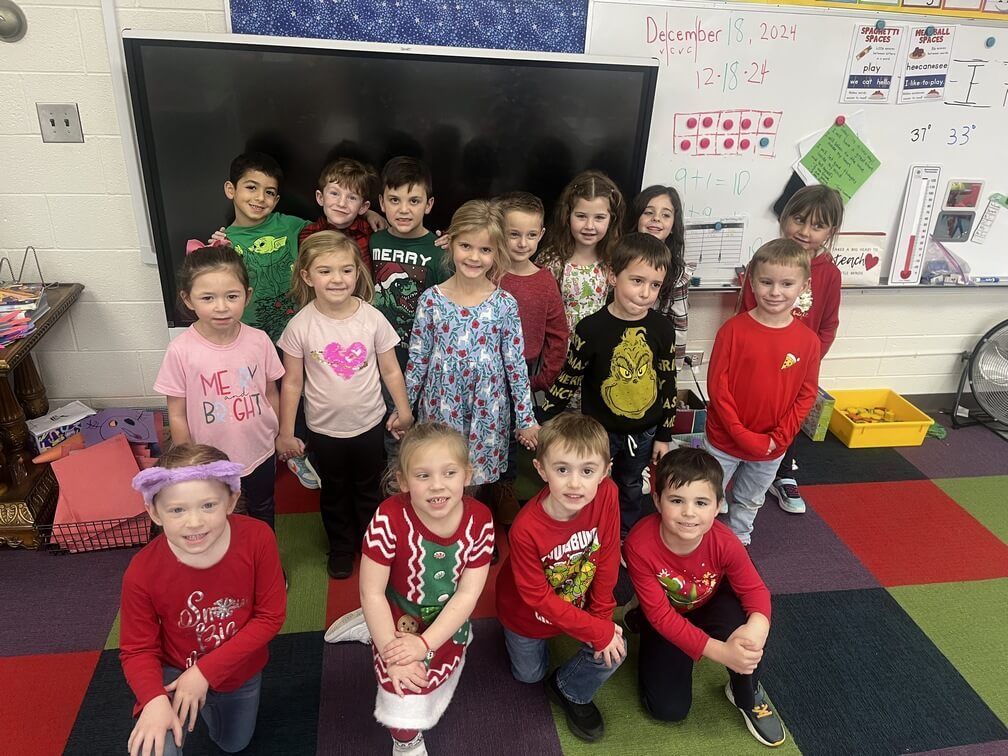 Children in holiday attire pose for a class photo in a classroom.