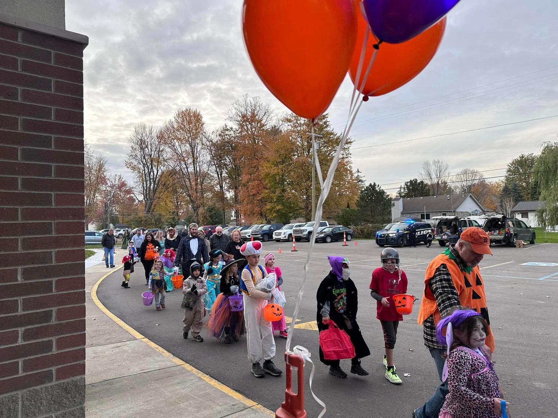 A group of children and parents in Halloween costumes walking towards the school.