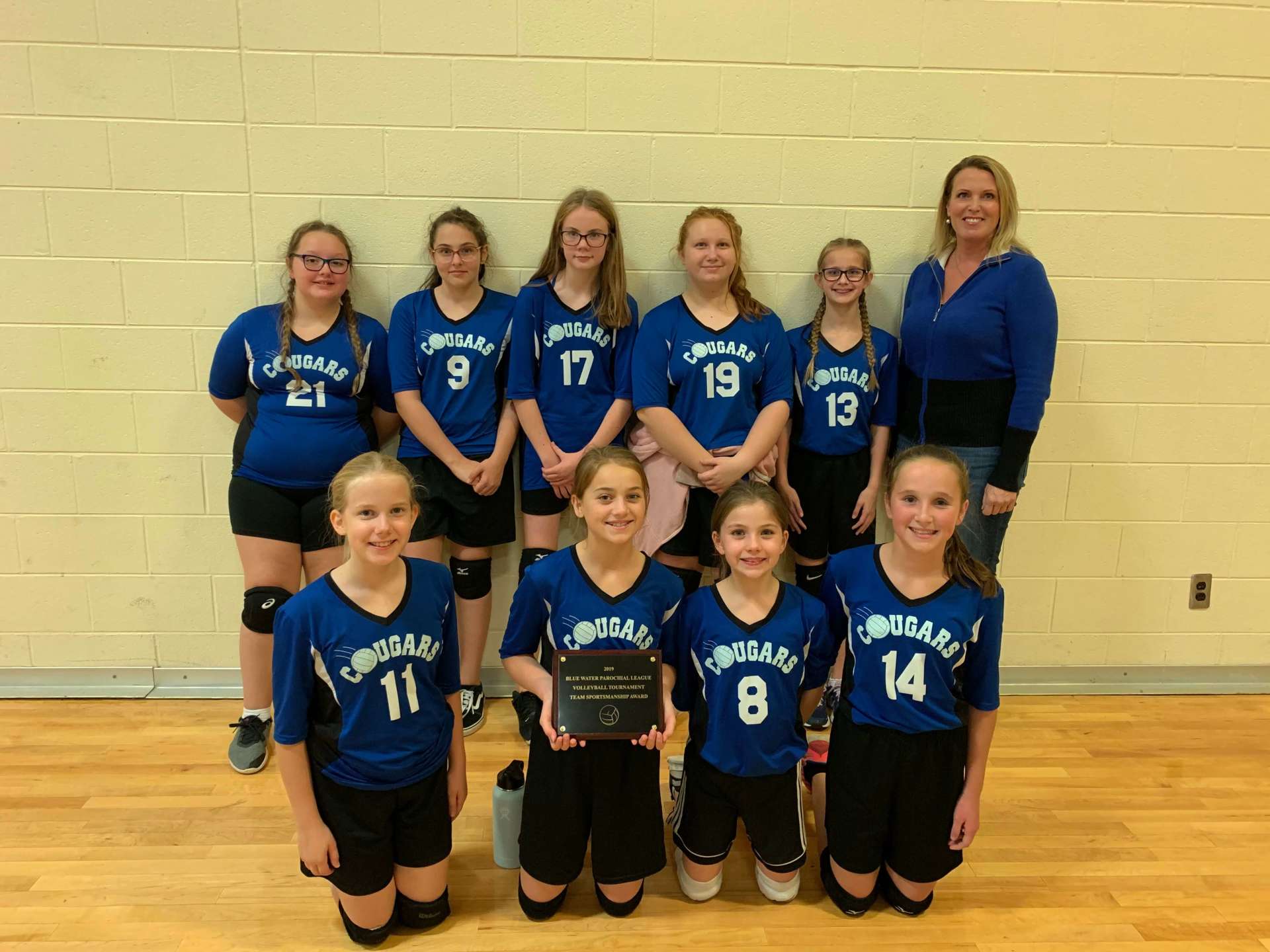 A group of girls wearing Cougars jerseys pose for a picture with a plaque.