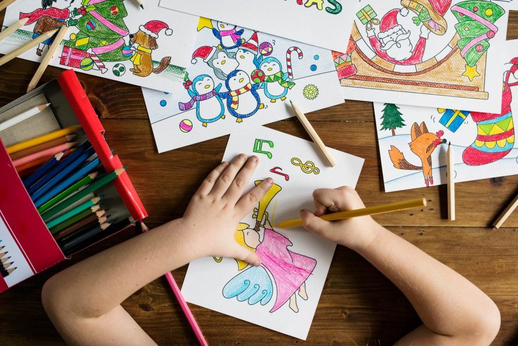 A child is sitting at a table drawing with colored pencils