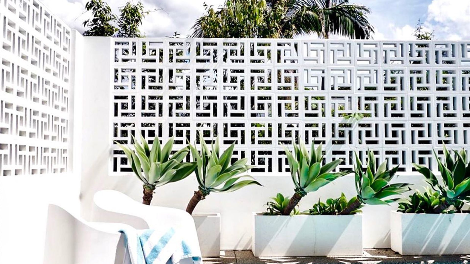 A white wall with a pattern on it is surrounded by plants and a chair — Premier Bricks, Blocks & Pavers In Heatherbrae, NSW