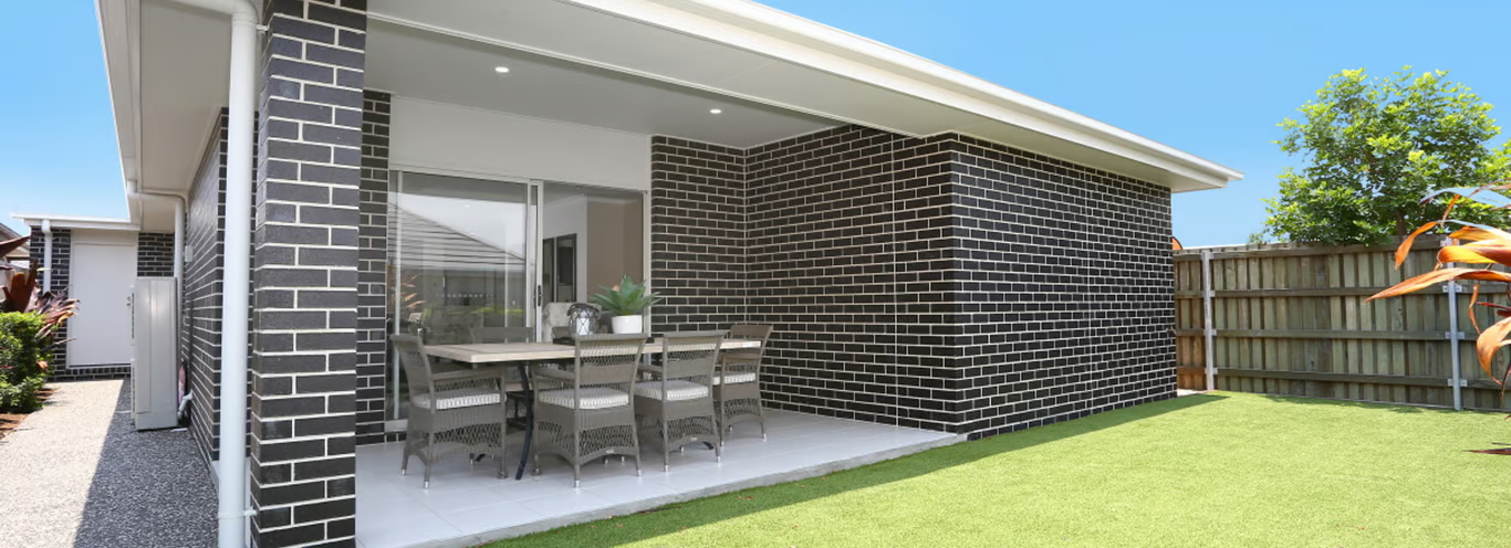 Backyard patio with brick walls, dining table, and green lawn — Premier Bricks, Blocks & Pavers In Heatherbrae, NSW
