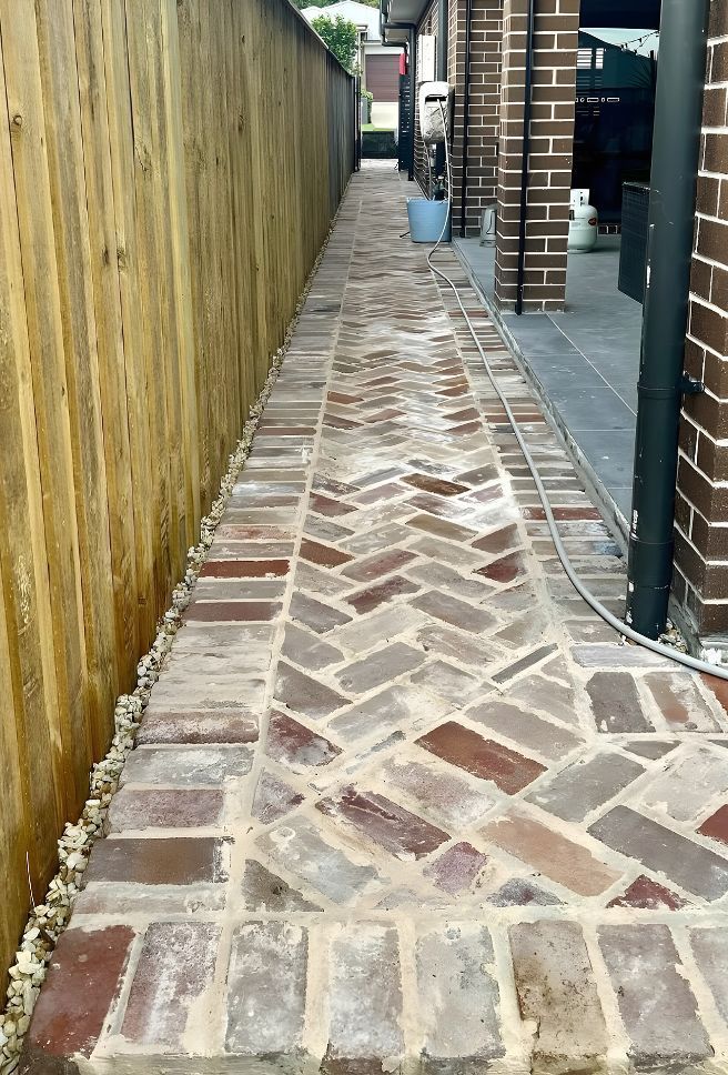 A Brick Walkway Leading To A House With A Wooden Fence — Premier Bricks, Blocks & Pavers In Chisholm, NSW