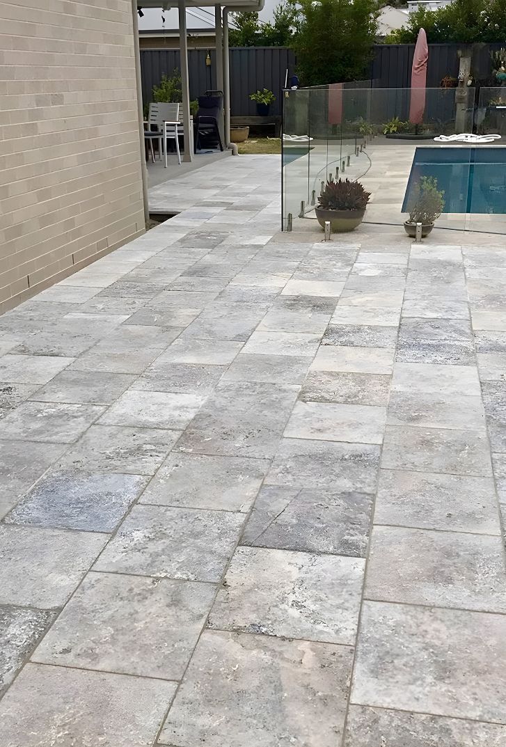 A Tiled Patio With A Swimming Pool In The Background — Premier Bricks, Blocks & Pavers In Maitland, NSW