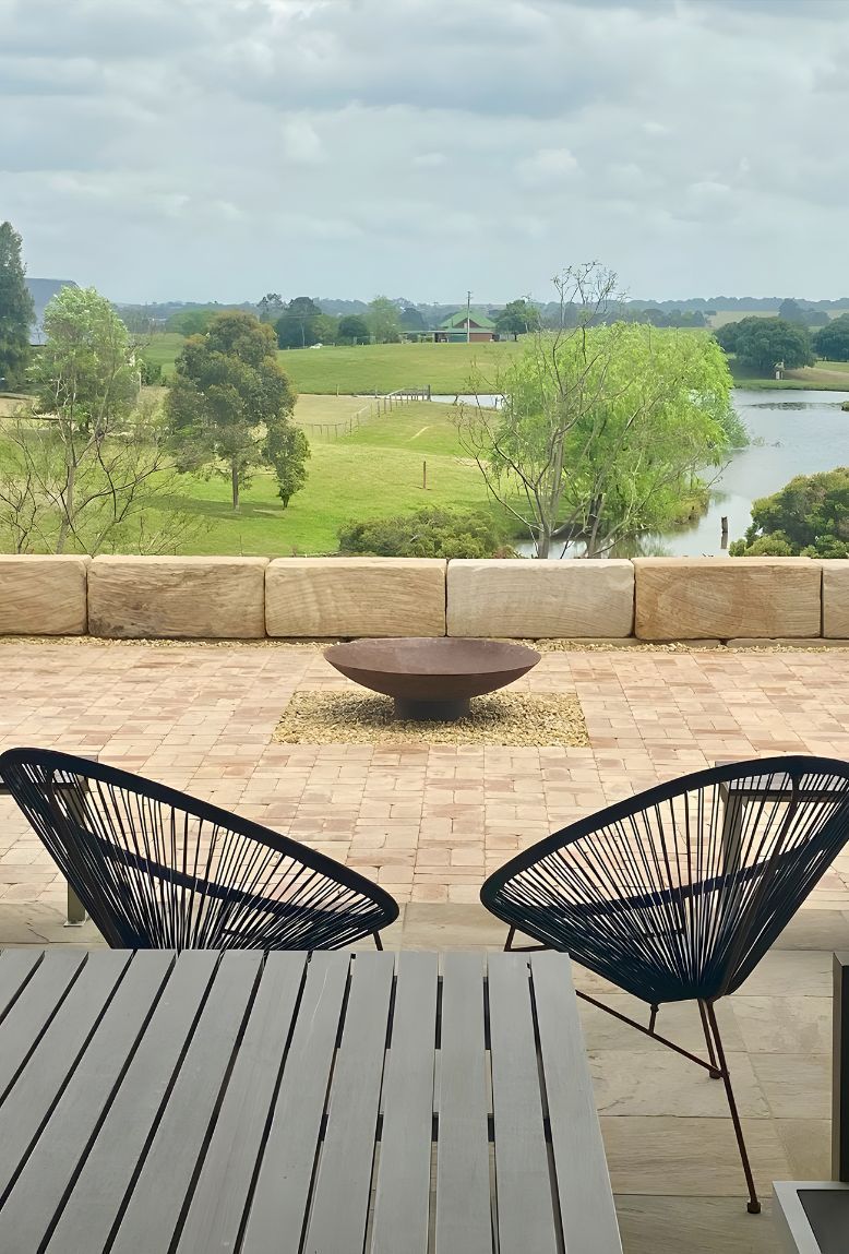 A Table And Chairs On A Patio With A View Of A River — Premier Bricks, Blocks & Pavers In Singleton, NSW
