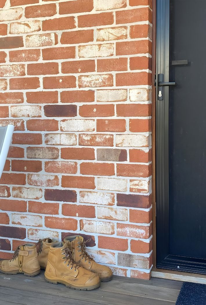 A Pair Of Work Boots Are Sitting On A Porch Next To A Brick Wall — Premier Bricks, Blocks & Pavers In Lake Macquarie, NSW