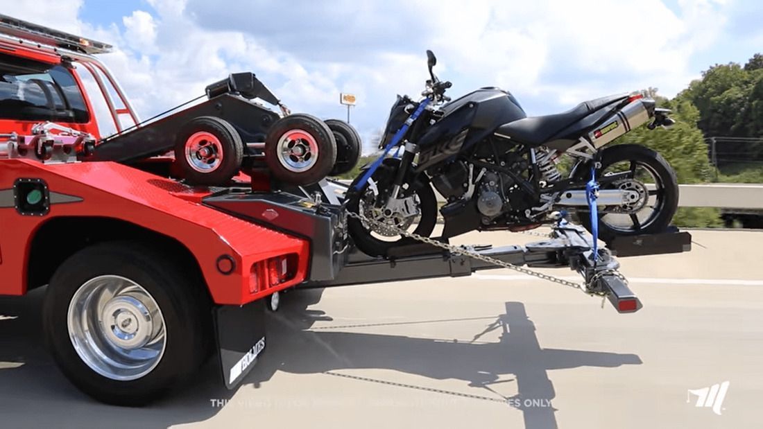 Motorcycle being towed on a flatbed tow truck on a highway. The truck is red.