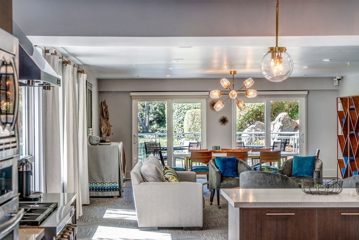 Open-concept living area with kitchen island, seating, and dining table by glass doors to a balcony. View our 1- and 2-bedroom homes and townhomes at Finch at Larkspur in scenic Larkspur, CA.  