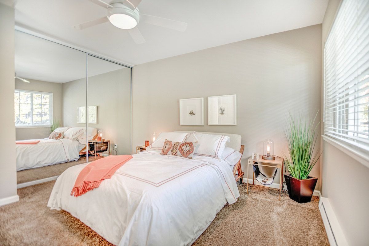 Bedroom with a neatly made bed, mirrored closet doors, two nightstands, and a potted plant. View our 1- and 2-bedroom homes and townhomes at Finch at Larkspur in scenic Larkspur, CA.  